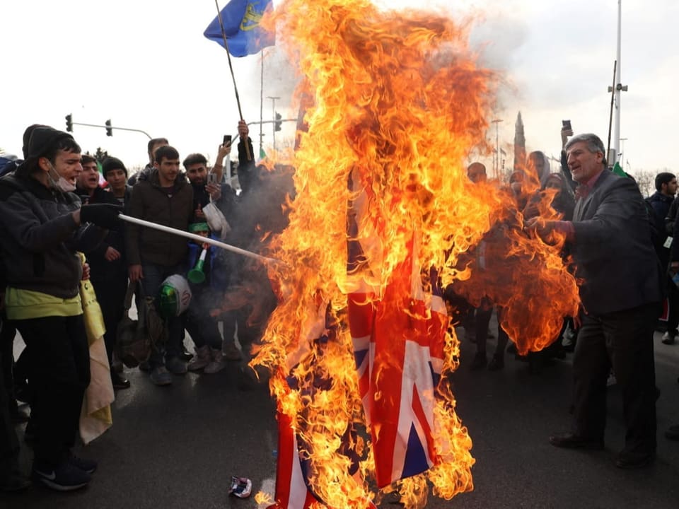 Männer stehen im Kreis um brennende Flaggen der USA und von Grossbritannien.