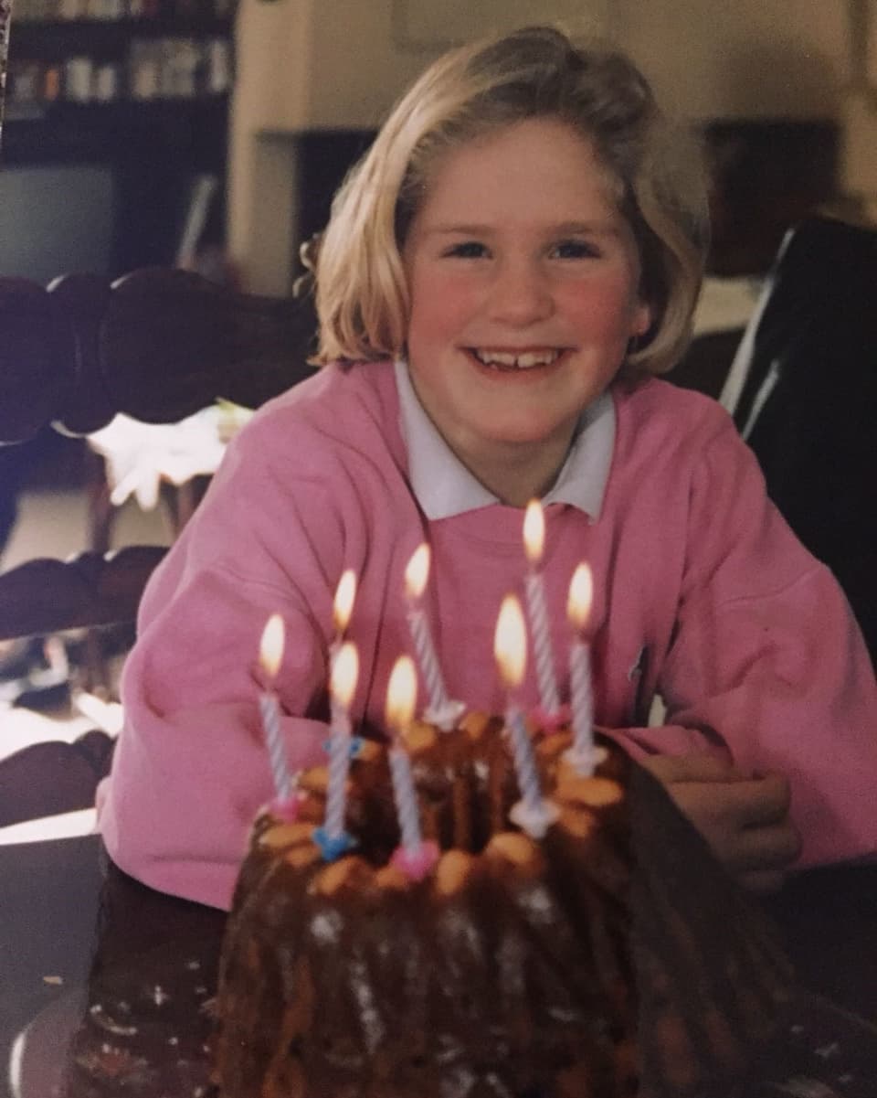 Ein blondes Kind sitzt vor einem Gugelhopf mit acht Kerzen.