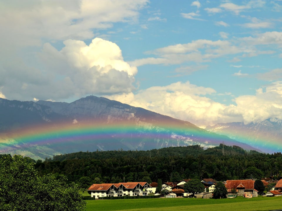 Flacher Regenbogen vor Bergkulisse.