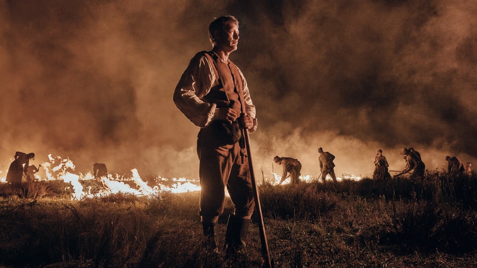 Mann steht nachts im Feld, Hintergrund mit Feuer und Menschen.