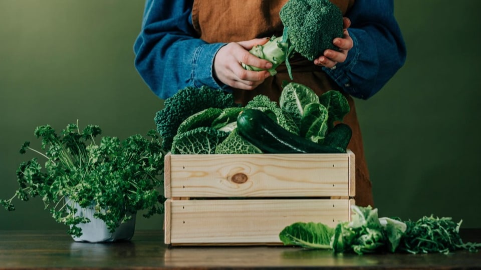 Eine Frau steht hinter einer Kiste voll Gemüse.