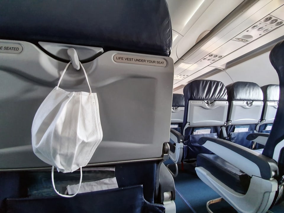 Eine medizinische Maske hängt an einem Sitz in einem Flugzeug.