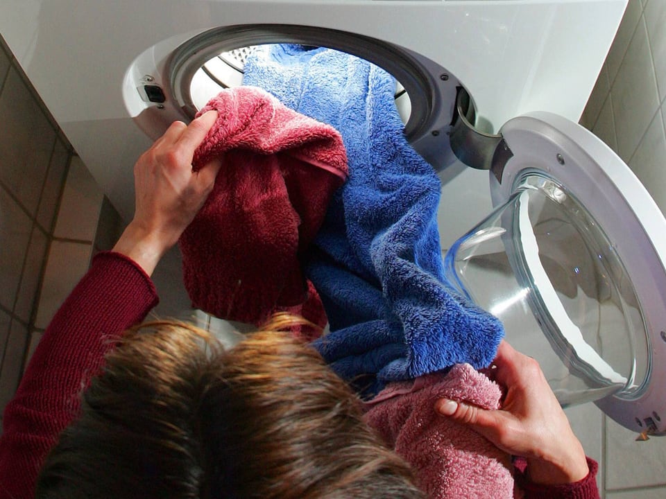 Frau kniet vor Waschmaschine und füllt sie.