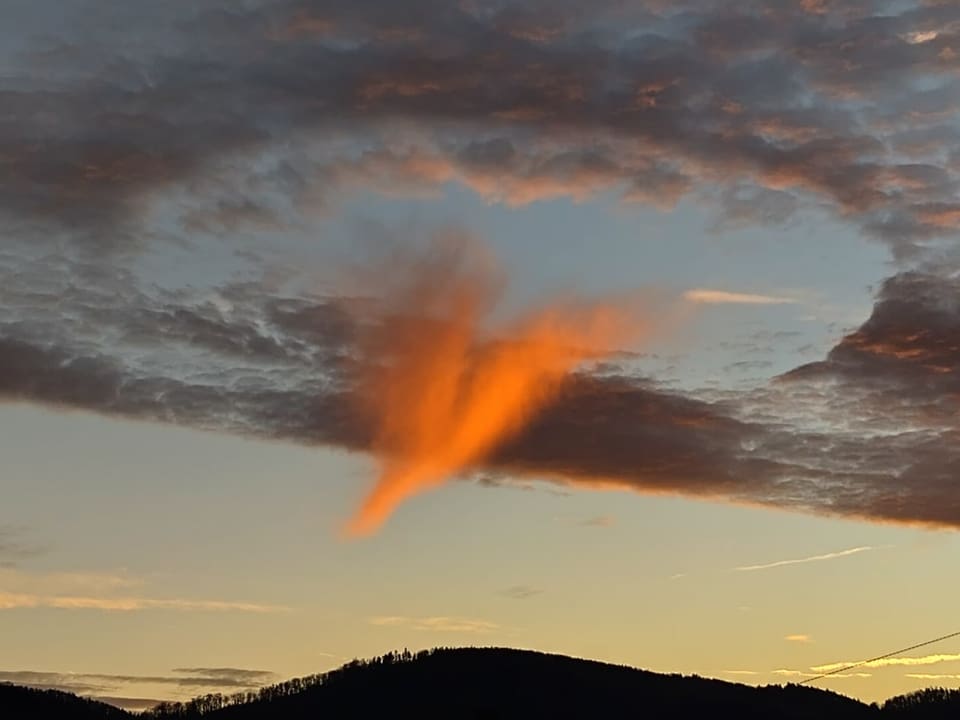 Wolkendecke mit Loch, darunter eine Wolke in Herzform, die von der untergehenden Sonne rötlich beleuchtet wird. 