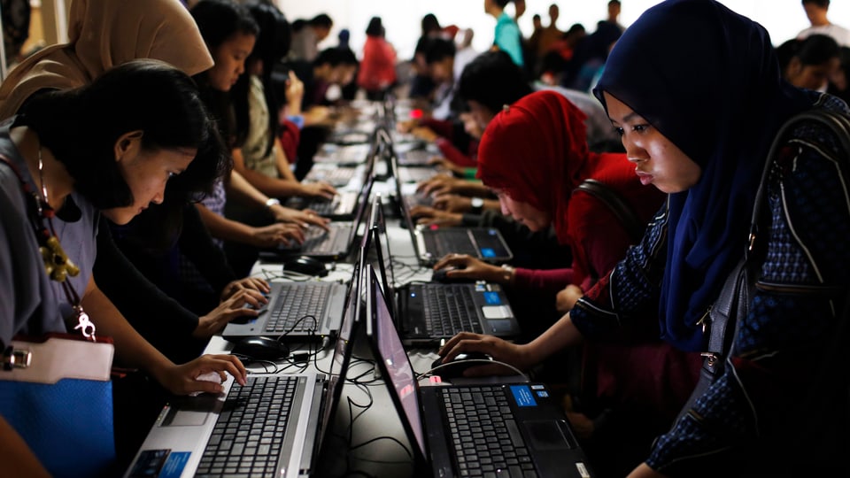 Junge Indonesier und Indonesierinnen füllen an Computern Bewerbungen aus. 