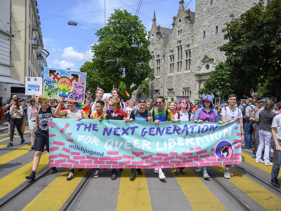Eine grössere Gruppe von jungen Menschen trägt ein grosses Transparent vor sich auf dem steht: For the next Generation, für queer liberation.