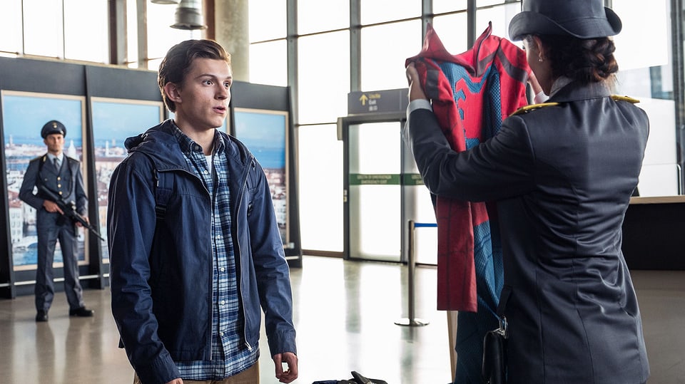 Eine Zollbeamtin hält einen Superhelden-Anzug hoch. Vor ihr steht ein geschockt dreinblickender Teenager..