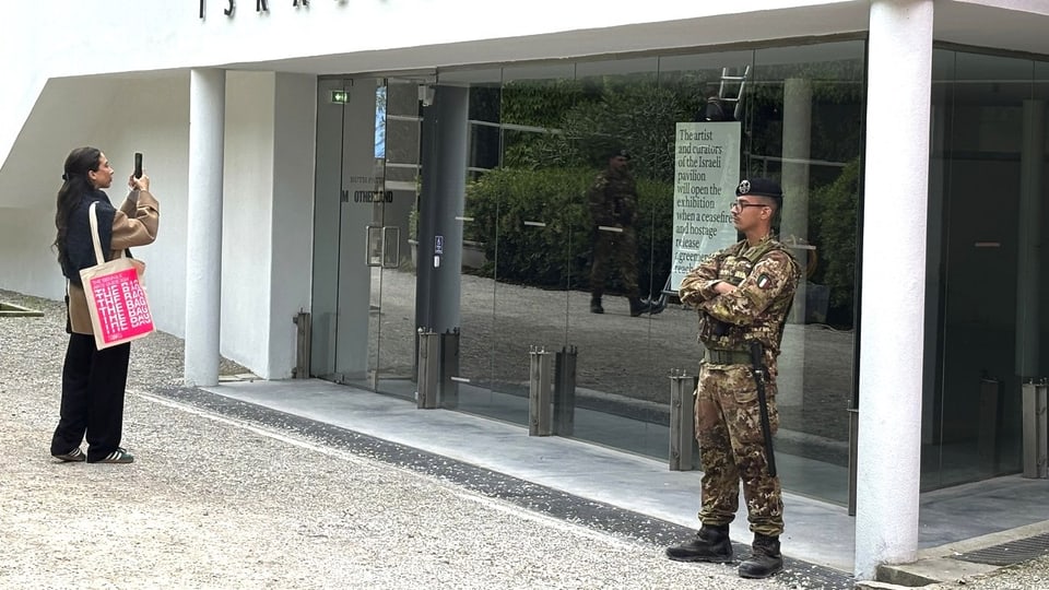 Eine Besucherin steht vor dem israelischen Pavillon in Venedig, zu ihrer rechten befindet sich ein Soldat.