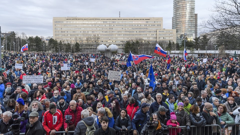 Menschen demonstrieren auf einem grossen Platz und schwenken die Flagge der Slowakei.