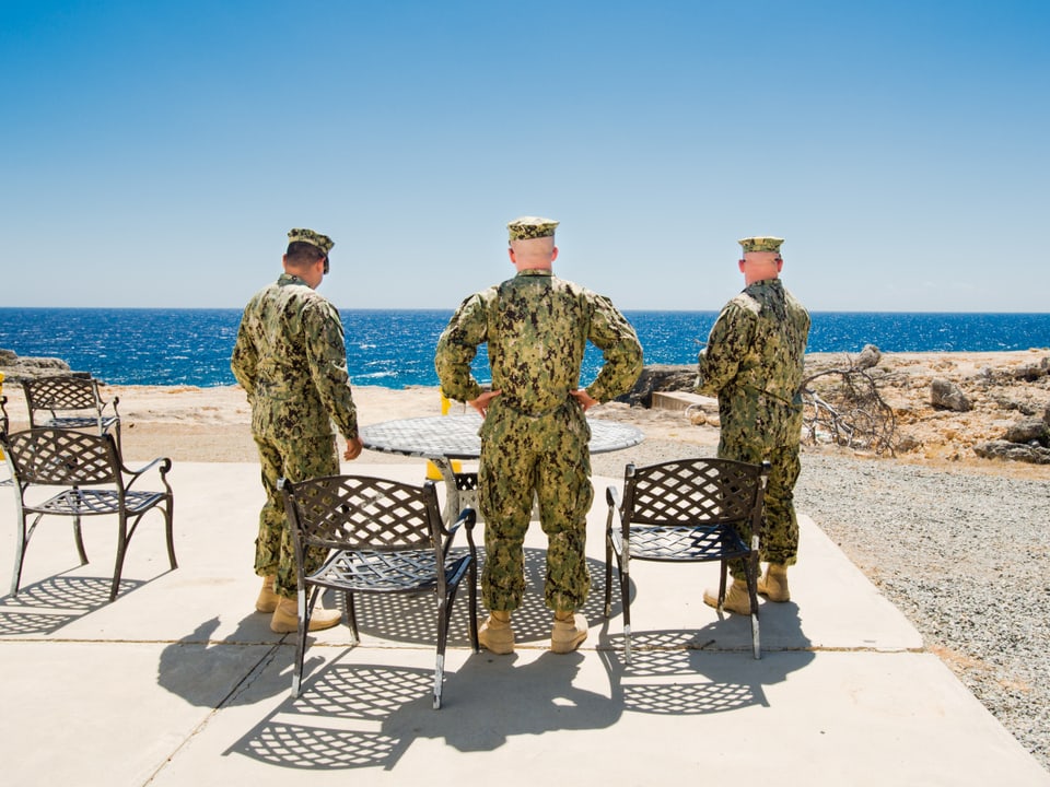Drei Soldaten von hinten fotografiert. Sie stehen am Strand und schaen aufs Meer.