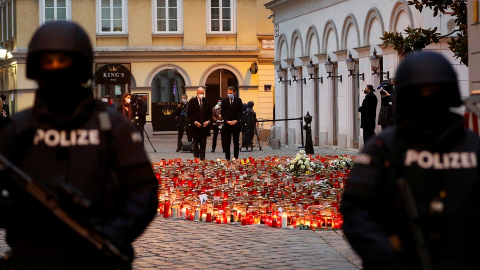 Zwei Polizisten bewachen den Tatort des Wiener Attentats, wo ein Kerzen- und Blumenmeer am Boden steht.