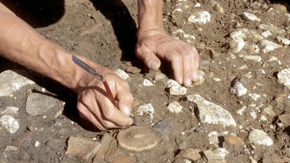 Ausgrabung: Mann putzt mit feinem Werkzeug Steine in der Erde.