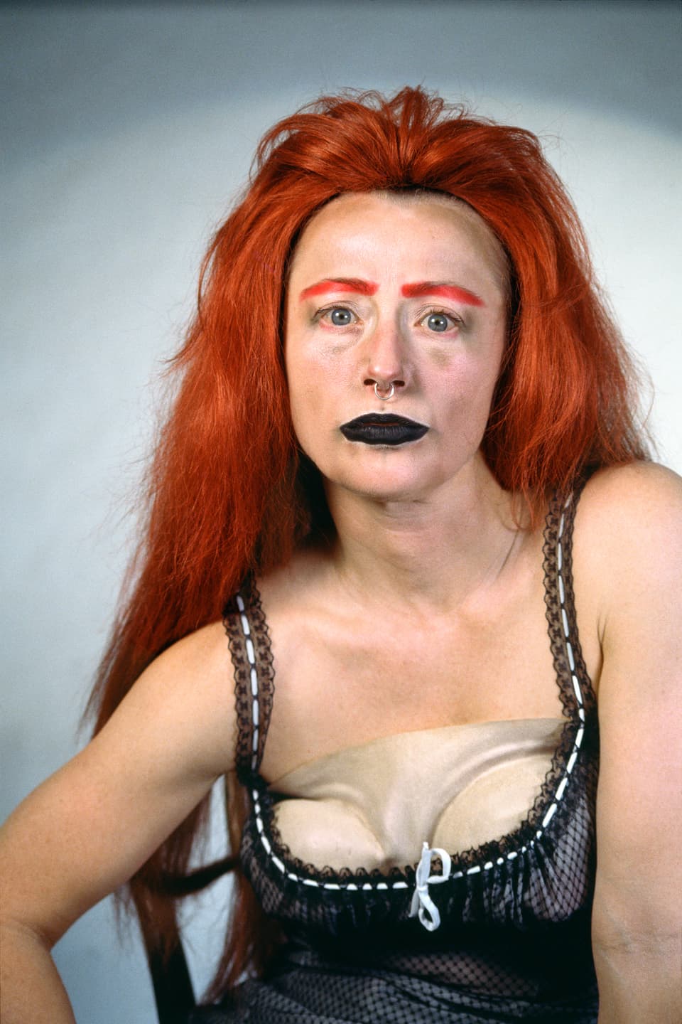 Eine Frau mit roten Haaren und Augenbrauen und schwarz geschminkten Lippen.