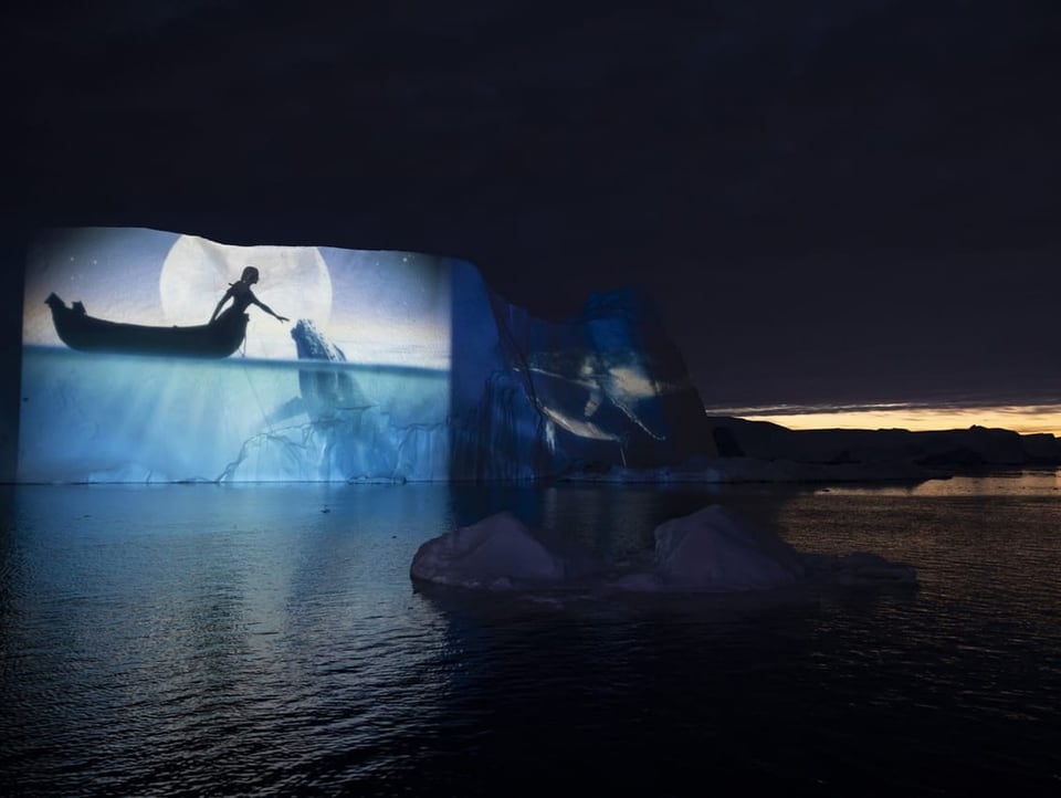 Eisberg beleuchtet mit dem Bild von einem Wal und dem Meer