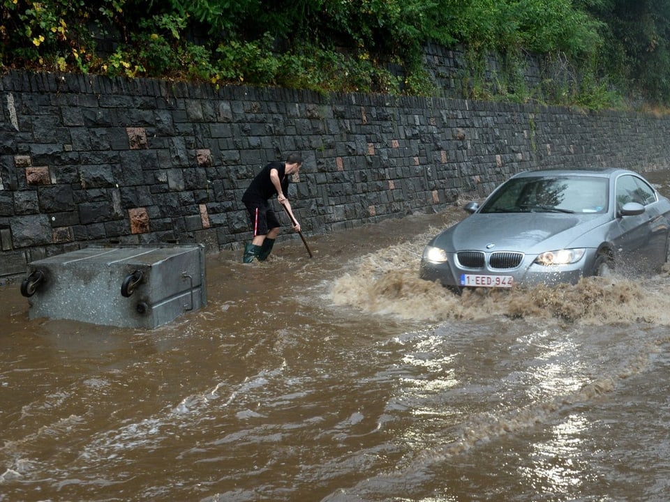 Auto und schaufelnder Mann im Hochwasser
