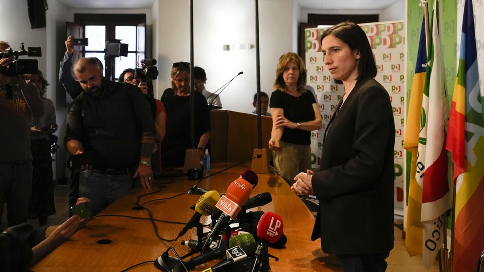 Elly Schlein umringt von Journalisten an einer Pressekonferenz.