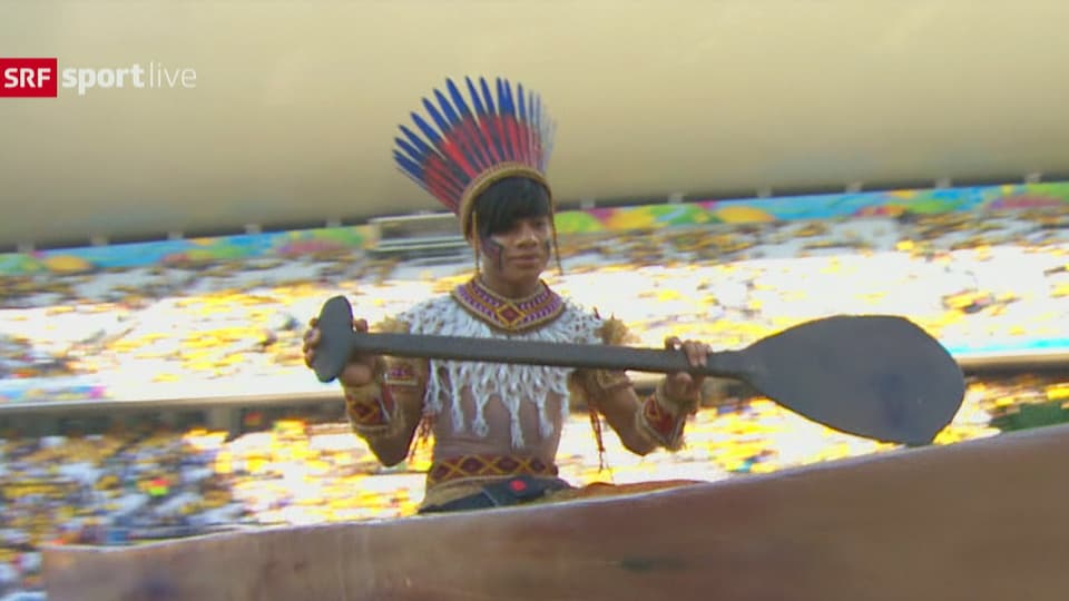 Eine Schauspielerin trägt ein Indigenen-Kostüm und sitzt in einem Paddelboot.