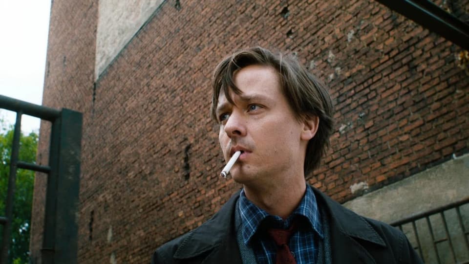 ein Mann mit Zigarette steht vor einer Wand