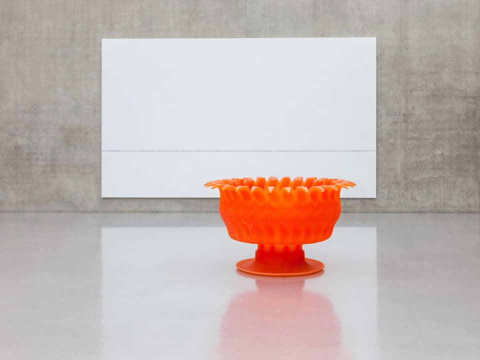 Ein oranges Objekt vor einer weissen Leinwand im Museum.