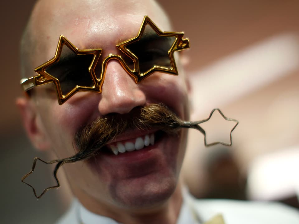 Ein Mann posiert mit einem Schnurrbart, der an seinen Enden zu zwei Sternen geformt wurde.