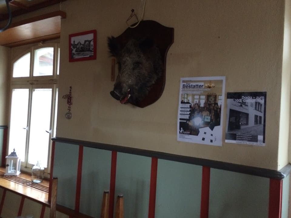Wand mit Plakat der Serie "Der Bestatter" neben einem aufgehängten Wildschweinkopf