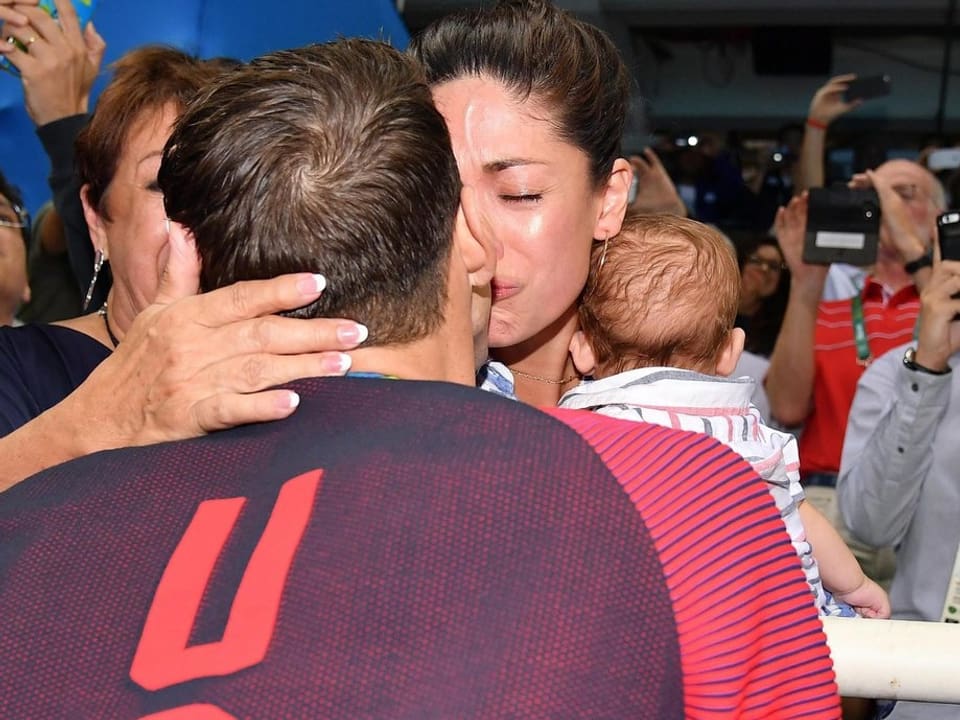 Michael Phelps küsst eine Frau, die ein Baby hält.