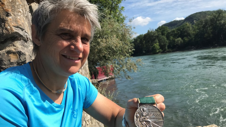 Sabine Eichenberger zeigt eine Medaille, im Hintergrund die Aare