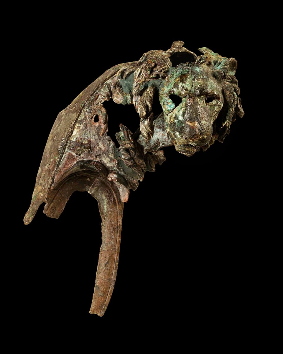 Ein bräunlich-grünliches Fragment mit einem Löwenkopf. 