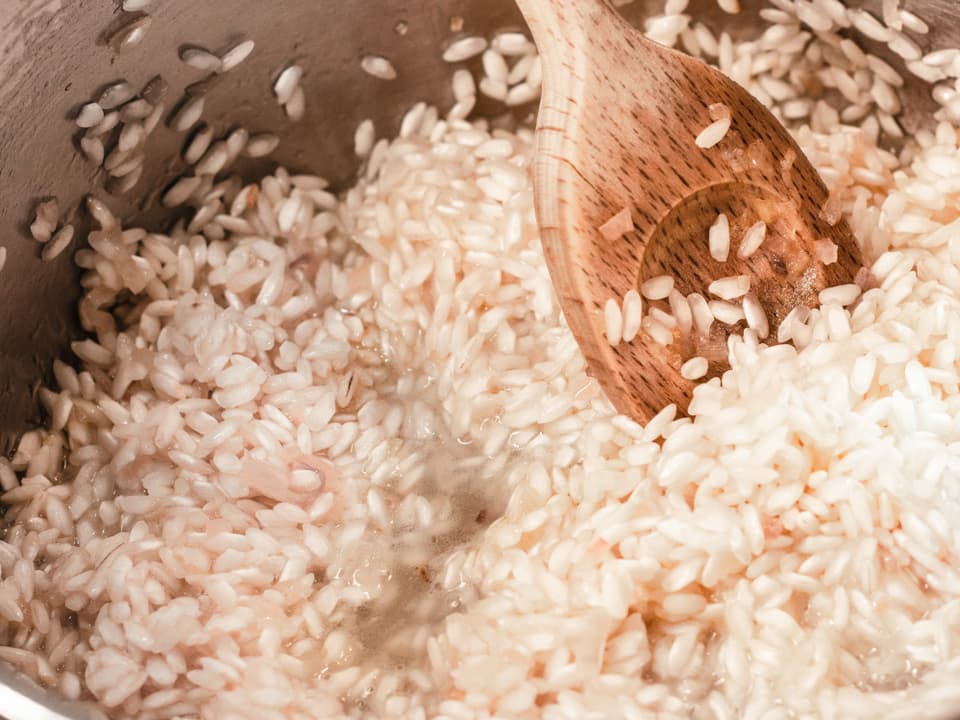 In einer Pfanne werden Risotto-Reis und gehackte Zwiebel mit Butter angedünstet. 