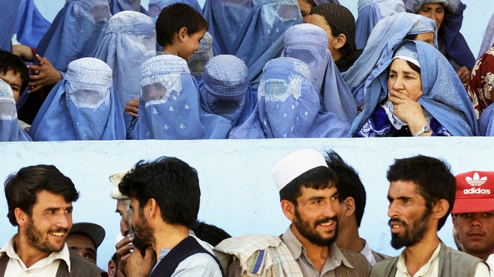 Männer und Frauen durch eine Mauer getrennt. Die Frauen tragen Burka.