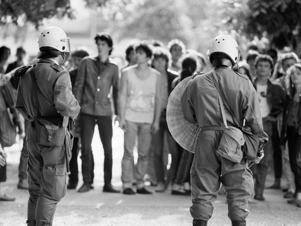 Polizisten in Kampfmontur vor einer Reihe Jugendlicher. 