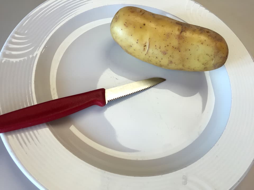 Kartoffel und Messer auf Schnittbrett.