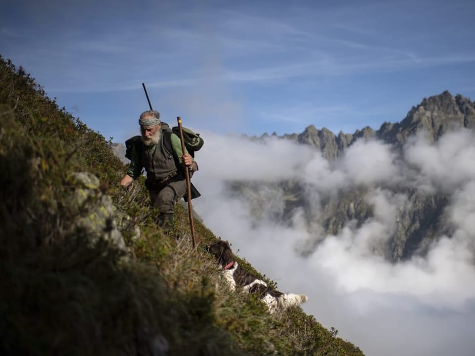 Ein Bündner Jäger pirscht mit seinem Jagdhund durch die Berge. 