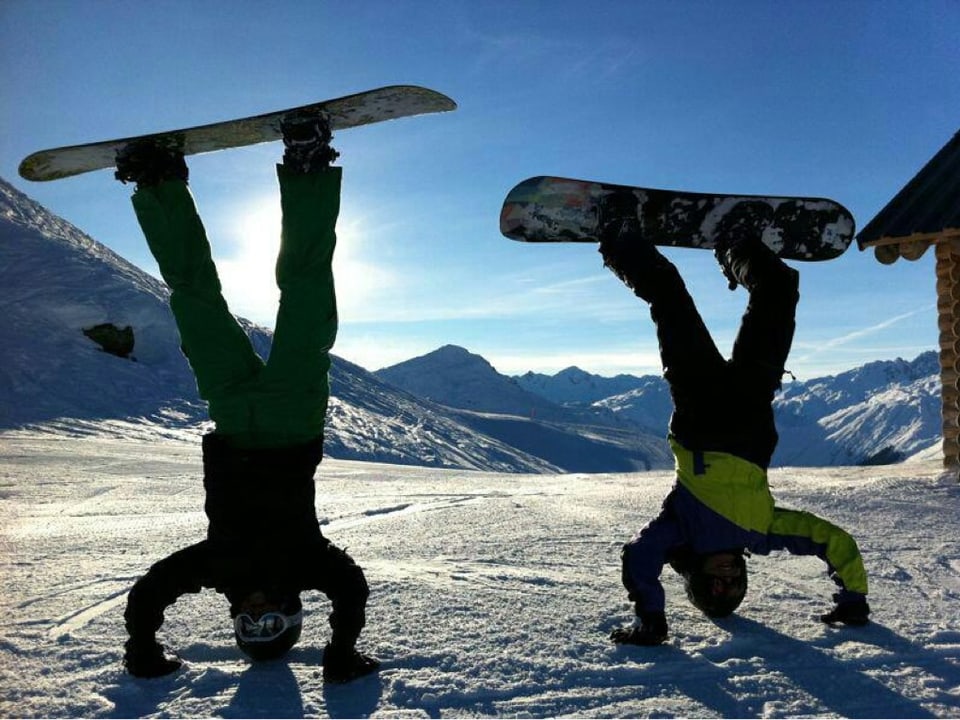 Zwei Snowboarder im Handstand.