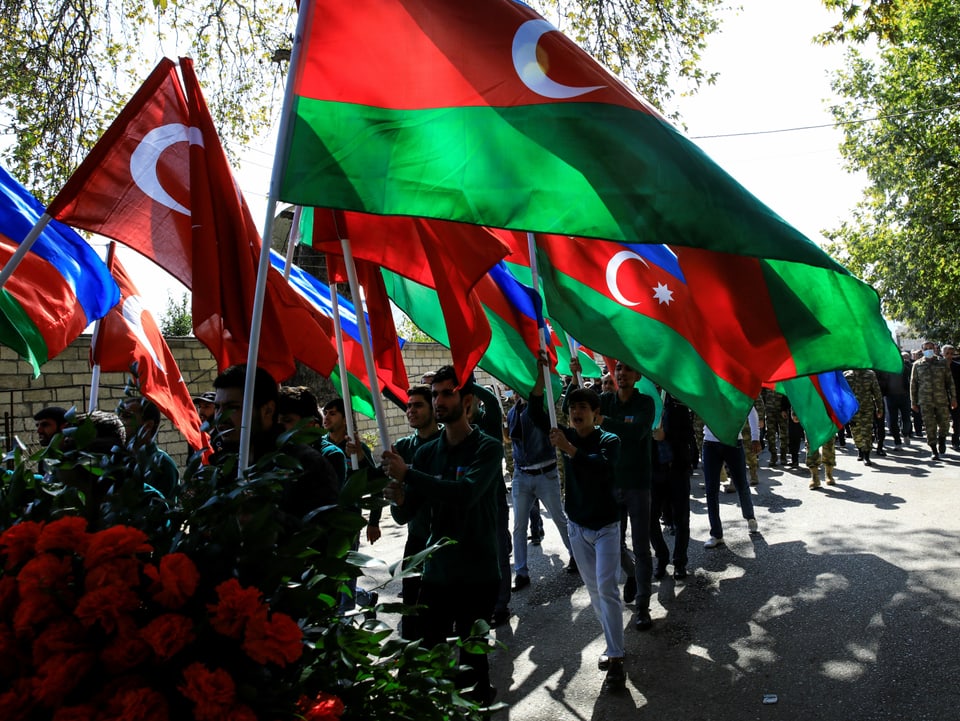 Menschen halten Flaggen von Aserbaidschan in die Höhe während eines Beerdigungsumzuges.