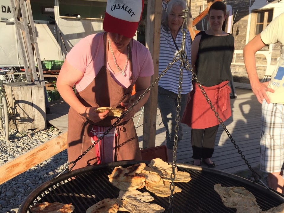 Sandra Knecht steht vor dem Grill, mit Grillwaren darauf. 