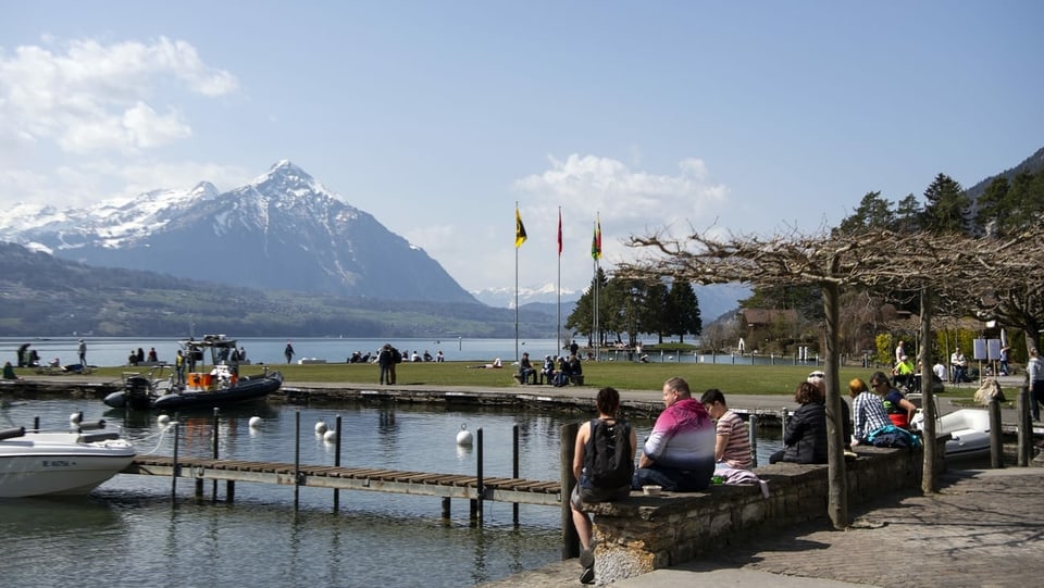 Leute sitzen in Interlaken am See auf Bänkli im Hintergrund der Niesen