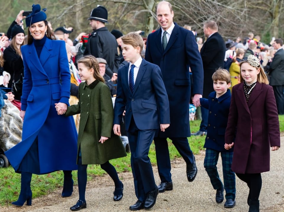 Prinz William und Prinzessin Kate gehen mit ihren drei Kindern und einem Mädchen einen Weg entlang.