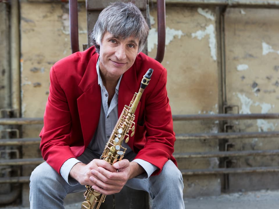 Musiker Daniel Schnyder sitzt in einem roten Anzug da und hält sein Saxophon in den Händen.