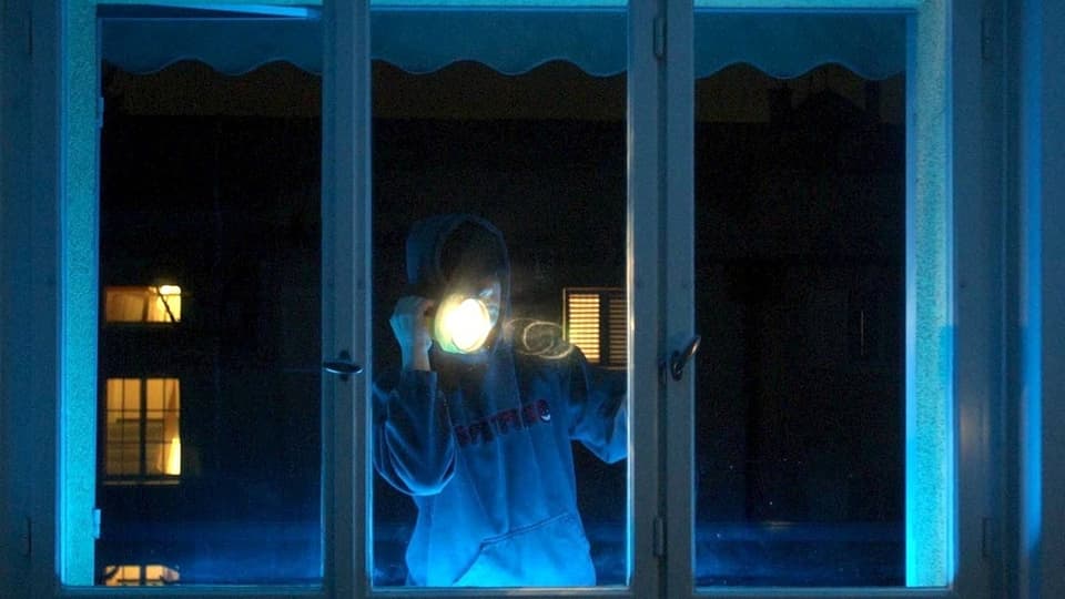 Ein Einbrecher leuchtet mit einer Taschenlampe in eine Wohnung.