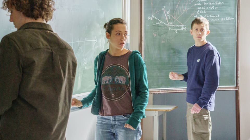 Drei Schüler diskutieren vor einer Tafel mit mathematischen Formeln im Klassenzimmer.