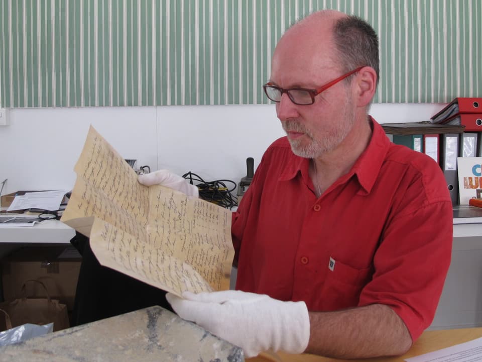 Mann mit Brille und weissen Handschuhen liest in einer alten Schrift