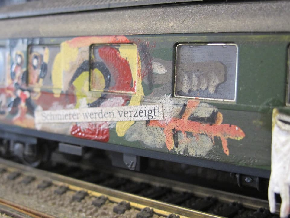 Ein Modellbahnwagen mit Sprayereien, darauf der Spruch "Sprayereien werden verzeigt"