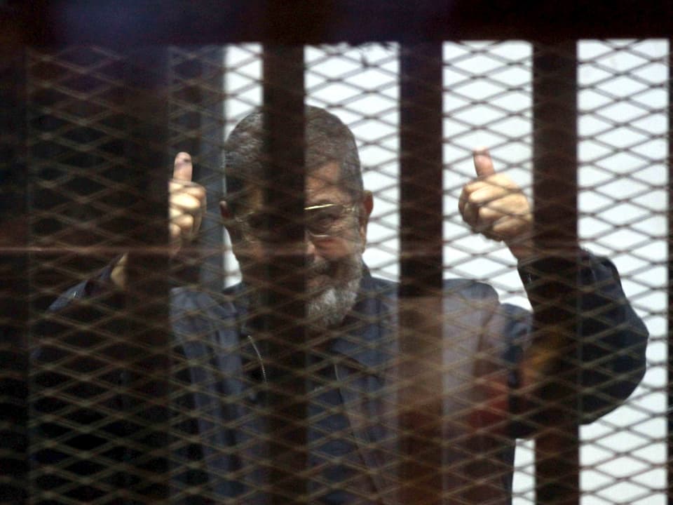 Mursi hinter Gittern mit erhobenen Daumen.