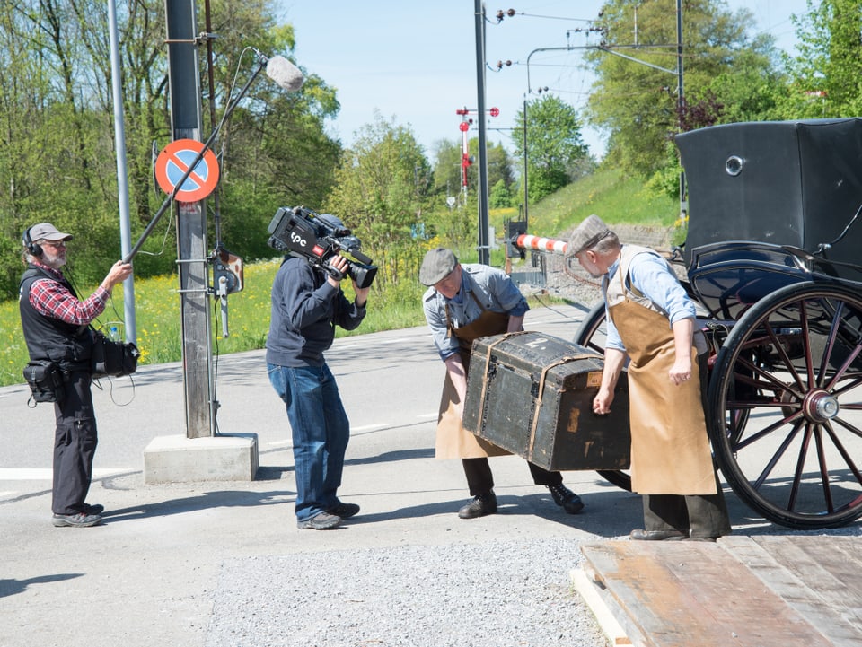 Kamerateam filmt zwei Helfer, die Koffer von Kutsche abladen