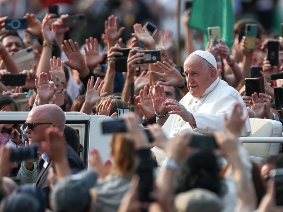 Der Papst sitzt im weissen Papamobil. Die Menschen rundherum halten Hände und Handys in die Höhe.