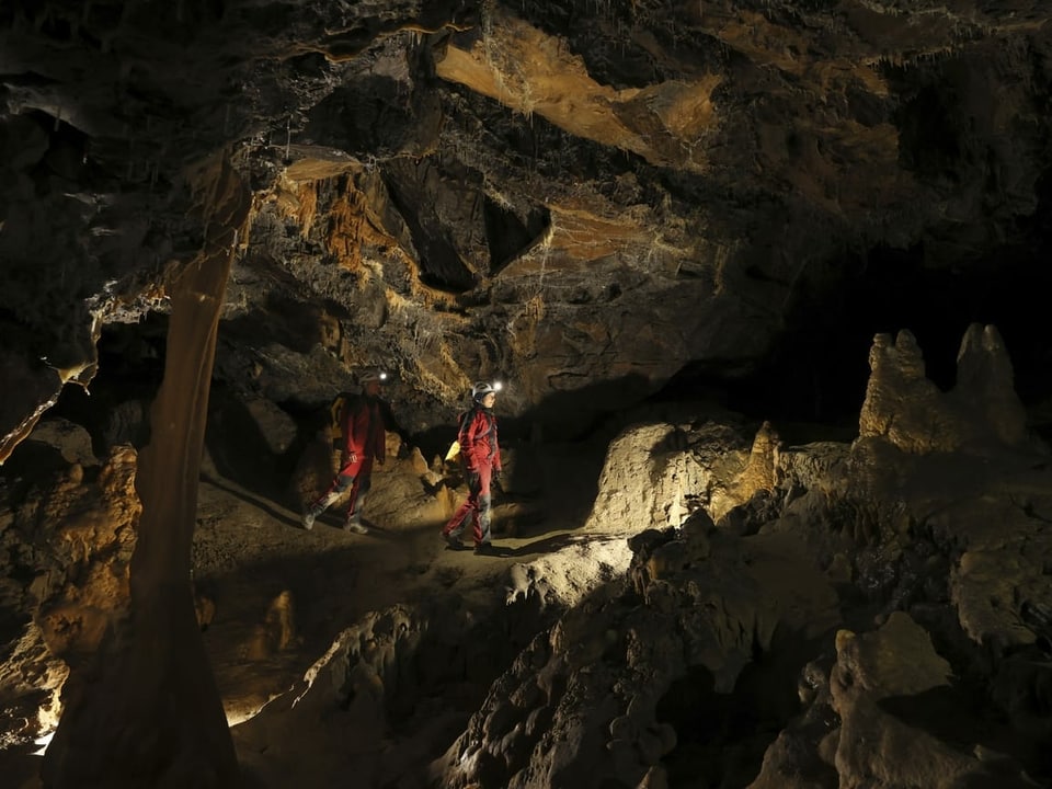 2 Teilnehmende erkunden die Höhle mit Stirnlampen.