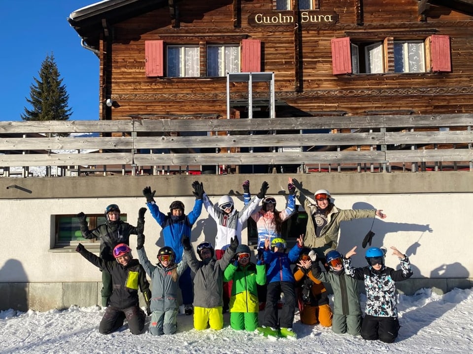 Eine Gruppe in Skiausrüstung posiert vor einem Lagerhaus