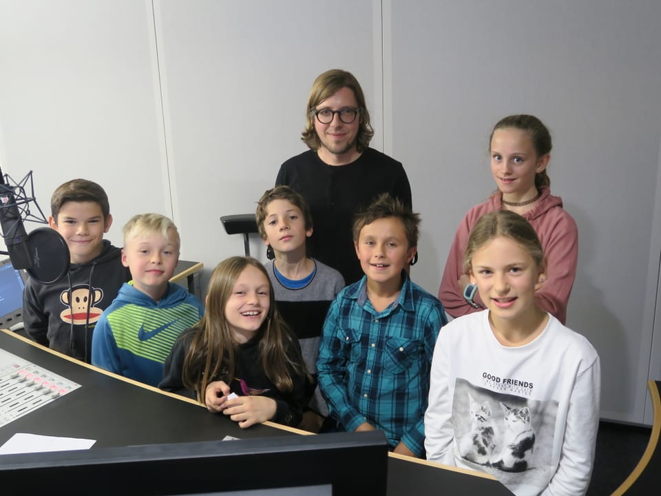 Sieben Kinder und ein Redaktor stehen hinter dem Sendepult im Radiostudio.