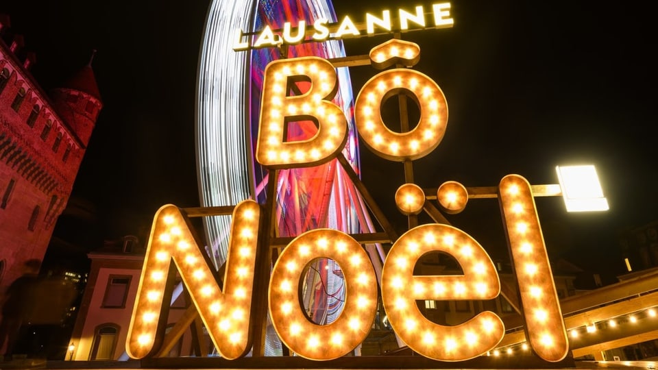 Grosse gelb-leuchtende Schriftzug mit «Bô Noël». Dahinter ein rot-weiss beleuchtetes Riesenrad.